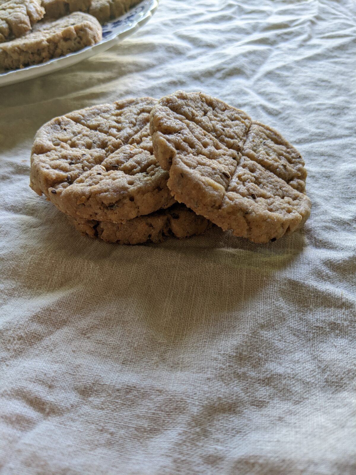 three stacked biscuits on a linen surface with a plate of more biscuits in the background