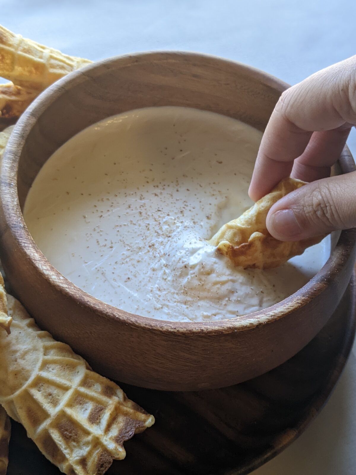 the author's hand dips a waffle-like biscuit into a bowl of sack cream